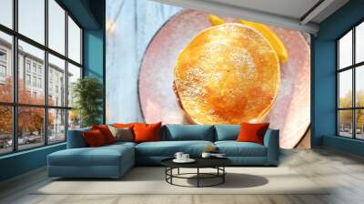 Pancakes with icing sugar and orange. Pancakes in a beautiful pink plate on a light wooden background. Delicious sweet food. Holiday pancakes and Christmas garland on the background. Wall mural