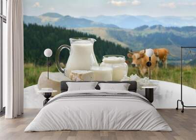 Milk, sour cream, cheese and cottage cheese on white table on background of meadow with cows in the mountains Wall mural