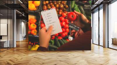 woman follows shopping list when buying fruits and vegetables in supermarket. Wall mural