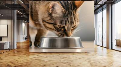 A playful tiger-striped cat eating from a metal bowl indoors, perfect for pet-related content. Wall mural