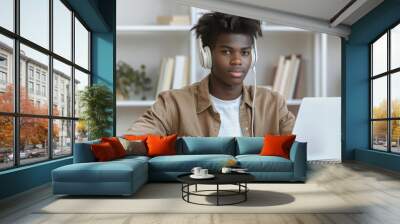 Focused teenage student using a headset to read a textbook during an online lesson at home, with a blank space for customization. Wall mural