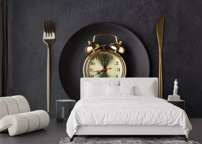 Golden alarm clock on a black plate with a golden knife and fork Wall mural