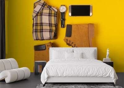 layout of autumn clothes and accessories in warm colors on a yellow background. Jeans, shirt, boots, phone and watch flat lay nearby Wall mural