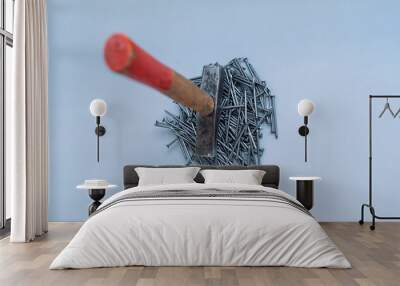 A hammer stands on a pile of nails in the middle of a gray background. Wall mural