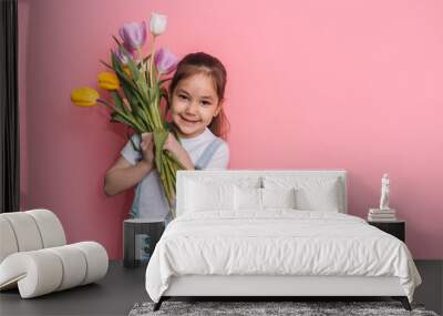 Child holding a bouquet of tulips in front of a pink background. Wall mural