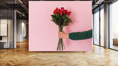 Female hand with bouquet of red roses against pink background. Wall mural