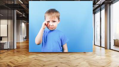 Upset crying sad boy at blue background, looking at camera. Wall mural