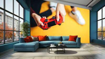 Young woman playing with two gamepads on yellow. Wall mural