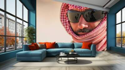 Close-up portrait of a bedouin man wearing traditional headscarf and modern sunglasses in a desert setting Wall mural