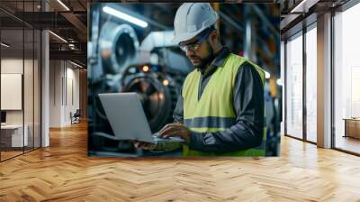 Focused engineer in safety gear using a laptop on the factory floor Wall mural