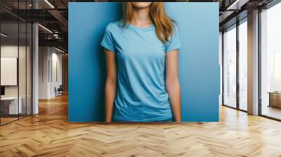 Young adult in a plain blue t-shirt poses against a solid blue background Wall mural