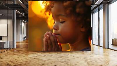 Young african american child with curly hair peacefully praying at sunset. Surrounded by the serene golden hour glow Wall mural