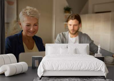 Business and cooperation concept. Successful middle aged female and bearded male manager working together at office, sitting in front of open laptop, having online business meeting using video chat Wall mural