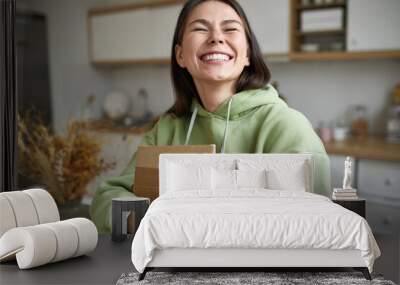 Cheerful teenage girl expressing positive emotions receiving unexpected birthday gift holding parcel and smiling with pleasure. Dark haired young woman posing with cardboard box with new cosmetics Wall mural