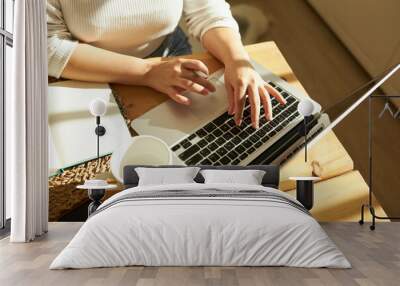 Cropped shot top view of female hands typing on keyboard of opened laptop at kitchen table with white coffee mug and notebook, studying online, checking e-mail, using learning application Wall mural