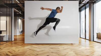 Endurance and stamina. Side view of athletic young Afro American sportsman training in studio, doing high jumps. Action shot of serious determined dark skinned male in sportswear jumping at white wall Wall mural