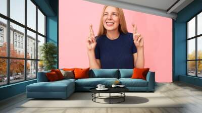 Good luck and superstition concept. Studio shot of emotional cute young woman with straight long hair keeping fingers crossed, hoping her dream come true, showing desire of favorable outcome Wall mural