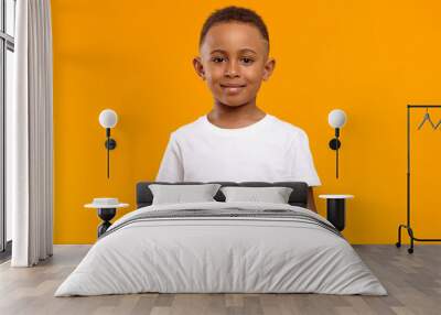 Isolated image of cute adorable dark skinned schoolboy wearing white t-shirt posing in blank yellow studio with confident cheerful smile because he received high marks for maths test at school Wall mural