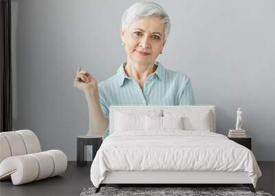 Isolated image of elegant fashionable middle aged European woman on retirement posing in studio wearing stylish striped blue shirt and wrist watch, having good day, smiling at camera happily Wall mural