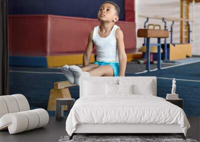 Picture of adorable dark skinned little gymnast competing on parallel bars. Hardworking talented African child exercising at gym, doing acrobatic moves, demonstrating strength, agility and flexibility Wall mural