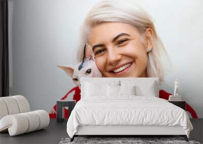 Picture of adorable young Caucasian female wearing trendy knitted pullover hugging her cute highbred pet. Sphynx cat with no fur purring in arms of her happy teenage female owner. Pets and people Wall mural