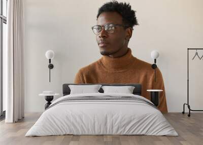 Portrait of fashionable creative young black male freelancer posing isolated in stylish spectacles and sweater having great idea while working on new project, looking up with thoughtful smile Wall mural