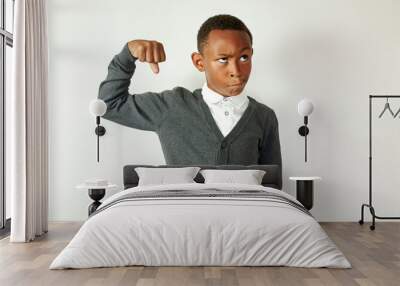 Portrait of funny black male school kid in gray cardigan and formal shirt making faces pretending being bodybuilder, showing bicep, looking up grimacing, isolated on white studio background Wall mural