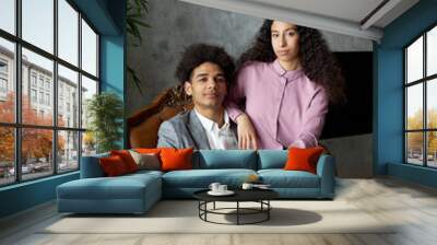 Portrait of young successful confident african american businessman start-upper sitting in armchair in suit with her gorgeous stylish elegant latin girlfriend on lap in fabulous home interior Wall mural