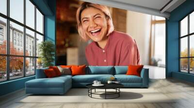 Positive human emotions and facial expression. Attractive casually dressed young female in her twenties burst out laughing, expressing genuine reaction, having fun in stylish cozy apartment Wall mural