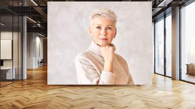 Serious pensive middle aged female wearing warm pullover and pearl earrings looking at camera having deep in thoughts facial expression, holding hand under chin. Contemplation and deliberation Wall mural