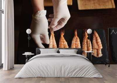 Closeup view of woman's hands in gloves are preparing shrimp for rolling sushi in restaurant Wall mural