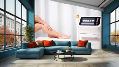 Cropped photo of beautiful female legs after laser hair removal procedure. On white background slender naked legs on couch next to laser hair removal machine. Aesthetic medicine concept. Wall mural