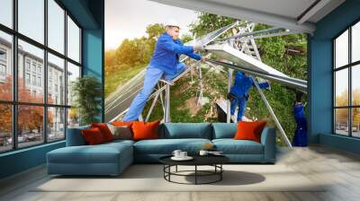 Installing of stand-alone solar photo voltaic panel system. Two technicians in hard-hats mounting big shiny solar module on platform on green summer view background. Alternative energy concept. Wall mural