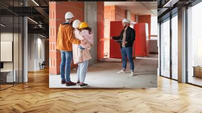 Man and woman with child standing inside apartment building under construction and talking with builder. Family future homeowners discussing building process with construction worker. Wall mural