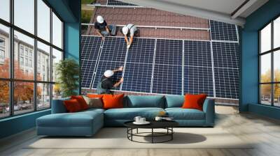 men technicians mounting photovoltaic solar moduls on roof of house. electricians in helmets install Wall mural