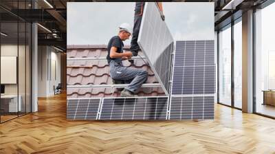 Men technicians mounting photovoltaic solar moduls on roof of house. Engineers in helmets installing solar panel system outdoors. Concept of alternative and renewable energy. Wall mural