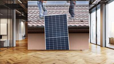 Men workers lifting up photovoltaic solar modul on roof of house. Electricians in helmets installing solar panel system outdoors. Concept of alternative and renewable energy. Wall mural