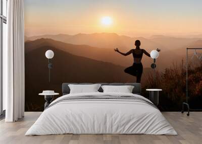 Panoramic view. Back view of slim woman in black sportswear doing yoga exercise on one leg in mountains. Concept of yoga time at sunset. Wall mural