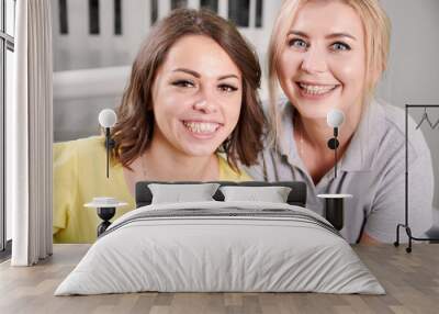 Portrait of two young beautiful women sitting in dental office. Orthodontist with her happy patient smiling at camera, demonstrating braces on their teeth. Concept of orthodontic treatment Wall mural