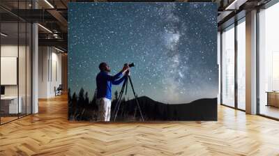 Professional photographer taking photos of Milky Way. Young male focusing his camera to take perfect picture of starry sky. Male taking pictures of night sky full of stars in mountains. Wall mural