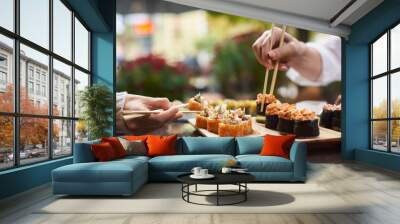 Two women sitting in asian restaurant and eating sushi set with help of chopsticks. Colleagues sharing tasty Japanese dinner with each other. Sisters enjoying oriental meal from rice and seafood. Wall mural