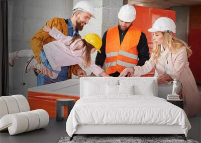 Woman standing next to builder and pointing at building plan while man holding daughter. Family with child discussing architectural plan of new apartment with construction worker. Wall mural