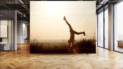 Young girl doing a handstand. Beautiful view horizon of a sunset on the background Wall mural