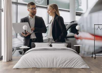 A male salesman showing something on a laptop to a female client buying a car inside a car dealership Wall mural