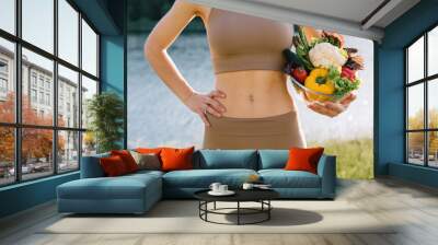 Female vegan holding plate of fresh vegetables near the belly in outdoors Wall mural