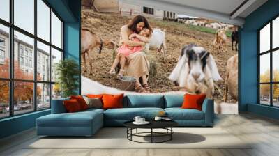 Happy mother and her daughter spend time on an eco farm among goats. Wall mural