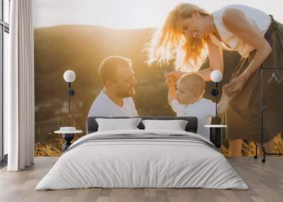 Joyful Family Outdoors: Parents Encouraging Baby's First Steps in a Sunlit Field Wall mural