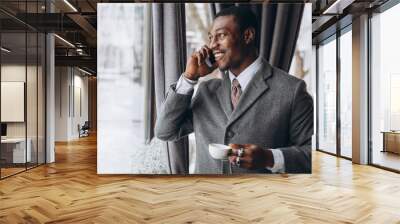 Modern african american businessman has a business conversation on a smartphone and drinking cup of coffee in restaurant. Wall mural