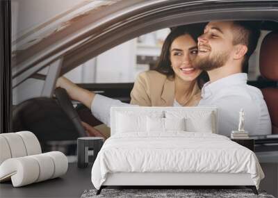 Portrait of smiling beautiful couple sitting in modern luxury car, happy excited young man and woman buying new car in dealership. Wall mural