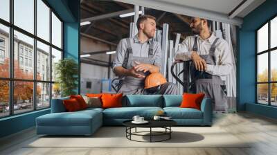 Portrait of two international workers wearing hardhats taking break from work and resting speaking to each other on a factory background with copy space Wall mural